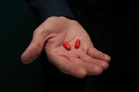 Young man in a dark shirt holding two red pillsの写真素材