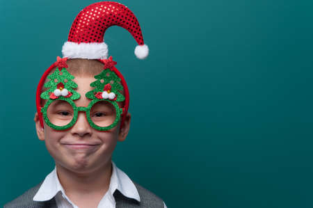 Portrait of happy cheerful boy wearing headband with Santa Claus Hat and funny glasses with Christmas treesの写真素材