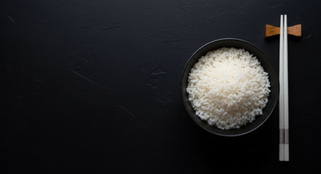 Bowl of rice and chopsticks on black background, top viewの素材
