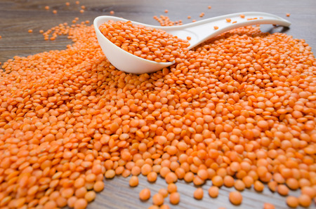 Orange lentils in a white spoon on a wooden table