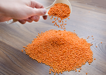 Red lentil pours from a white spoon on a wooden tableの写真素材