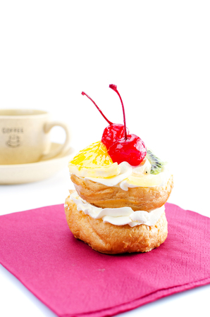 Choux pastry with fruit on burgundy napkin. Cherry, kiwi, orange and grapes. On a white background.の写真素材