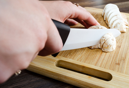 The girl cuts mushrooms on white chopping board of woodの写真素材