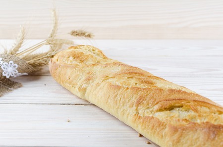 White fresh baguette is light on wooden boards. Spikelets of wheat wrapped in burlap.の写真素材