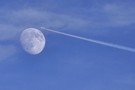  Jet stream of airplane going through the moon in blue sky の写真素材