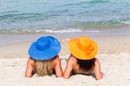 Back View of four young playful women in summer hats resting on the beach and enjoy the tropical sea. の写真素材