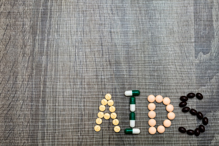 The word AIDS (Acquired ImmunoDeficiency Syndrome) written whith pills on a wooden background.の写真素材