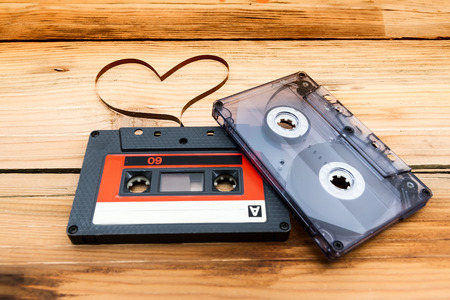Vintage audio cassette with loose tape shaping one heart on a wooden background.の写真素材