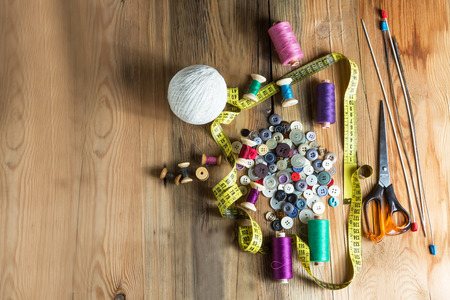 Sewing Supplies, Spools of thread, Buttons, Scissors, Measuring tape. On Wooden Background.