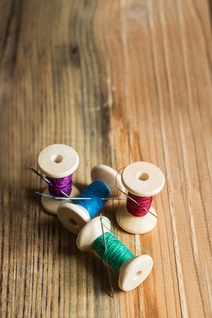 Spools of thread with needles on wooden background. Old sewing accessories. colored threadsの写真素材