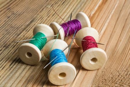 Spools of thread with needles on wooden background. Old sewing accessories. colored threads