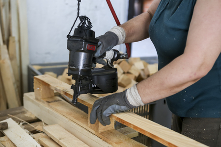 Thessaloniki, Greece, July 8, 2015: Craftsman puts nails in a piece of wood at a woodworking factory in Greece. Wood and furniture production plant, industrial factory with tools and objects.のeditorial素材