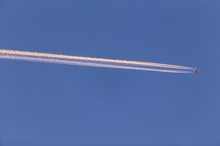 Airplane with contrail high in the sky at sunset