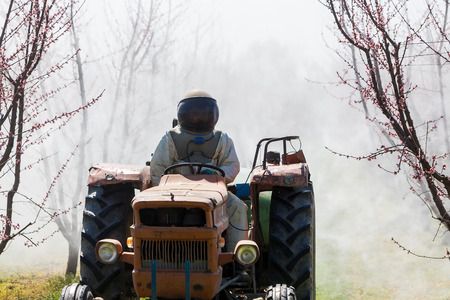 Veria, Greece - March 19, 2016: Farmer with tractor using a air blast sprayer with a chemical insecticide or fungicide in the orchard of peach trees in northern Greeceのeditorial素材