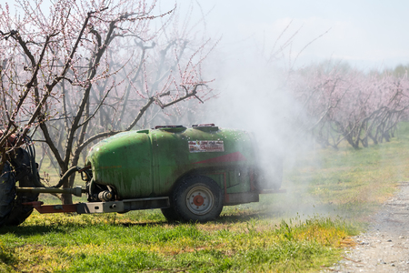 Veria, Greece - March 19, 2016: Farmer with tractor using a air blast sprayer with a chemical insecticide or fungicide in the orchard of peach trees in northern Greeceのeditorial素材