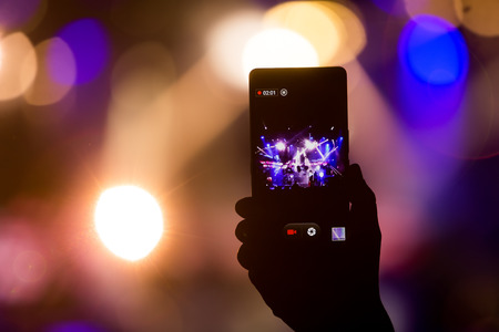 Hand with a smartphone records live music festival, Taking photo of concert stage, live concert,...