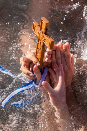 Thessaloniki, January 6, 2018: A close-up shot of the hands that retrieves a wooden cross in the...