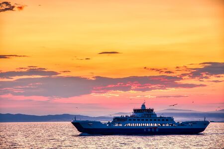 Thassos, Greece - July 20, 2019: Ferry boat to the sea at sunset in the background of mountains and sun beams, run from Keramoti city to Thassos island in Greeceのeditorial素材
