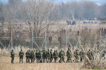 Kastanies, Evros, Greece - March 2, 2020: Greek police and soldiers in front of a fence trying to deter migrants as they attempt to enter Greece from Turkey at the Greek-Turkish border in Kastaniesのeditorial素材