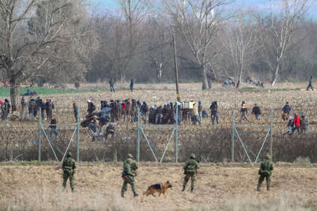 Kastanies, Evros, Greece - March 2, 2020: Greek police and soldiers in front of a fence trying to deter migrants as they attempt to enter Greece from Turkey at the Greek-Turkish border in Kastaniesのeditorial素材