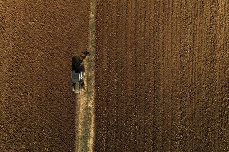 Aerial drone shot of a farmer in tractor seeding, sowing agricultural crops at field in the fertile...