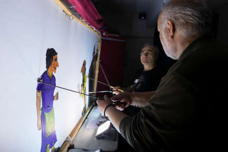 Thessaloniki, Greece - March 9, 2020: unidentified performers playing with the main character (Karagiozis) in the Greek shadow theatre behind the cotton screen during folk show.のeditorial素材