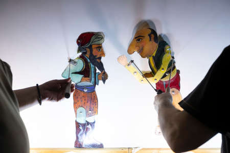 Thessaloniki, Greece - March 9, 2020: unidentified performers playing with the main character (Karagiozis) in the Greek shadow theatre behind the cotton screen during folk show.のeditorial素材