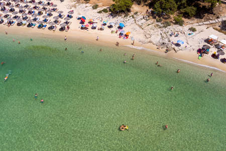 Psili Ammos, Thassos island, Greece - July 17, 2021: View from above, aerial view of an emerald and transparent Mediterranean sea with a white beach full of beach umbrellas and tourists who relax and swim.のeditorial素材