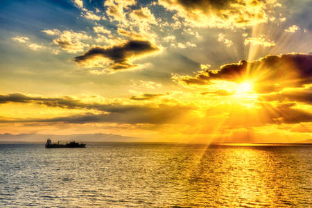 a silhouette of a cargo ship at sunset. Calm sea with sunset sky and sun through the clouds over. Meditation ocean and sky background.の写真素材