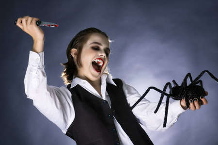 Boy dressed up as a vampire for halloween party, shouting while prepared to stab a spider toy with bloody knife.の写真素材