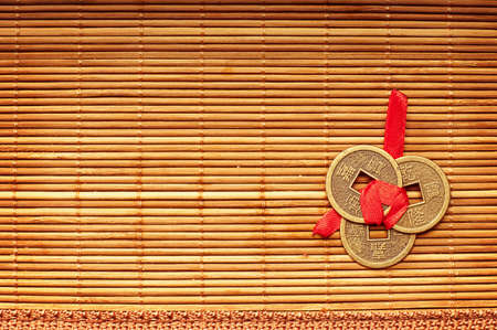 Three Chinese lucky coins tied with red ribbon on wooden matの写真素材