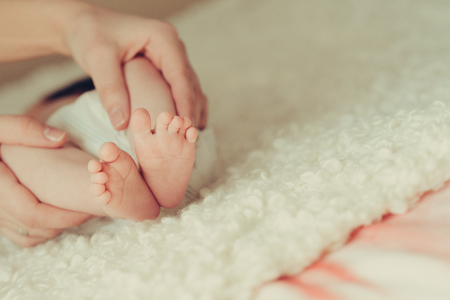 mothers hands holds baby feet at white blanketの写真素材
