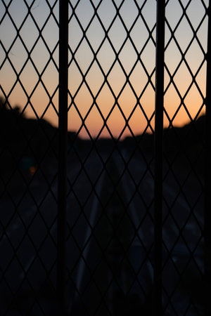 Silhouette of a wire mesh fence with traffic in the backgroundの写真素材
