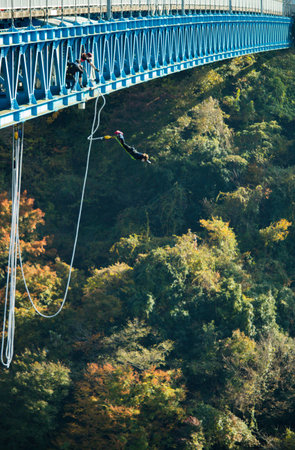 Bungee jumping from a suspension bridge over a river in autumnの写真素材