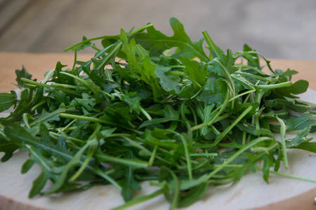 Green arugula leaves on wooden cutting board. Fresh rucola in the kitchen in plastic tray, Italian seasoning. Healthy lifestyle organic foodの写真素材