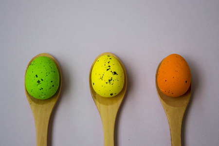 Colorful Easter eggs on pale pink background, egg in wooden spoons, green, orange, yellow, egg hunt...