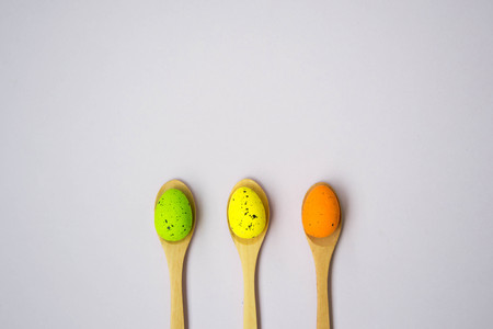 Colorful Easter eggs on pale pink background, egg in wooden spoons, green, orange, yellow, egg hunt...