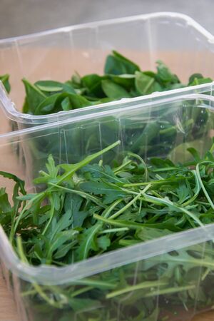 Close up of rukola leaves in  plastic containers on top of wooden table, in the kitchen, healthy eating, dieting, vegetarian lifestyle, food conceptの写真素材