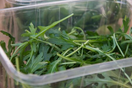 Close up of rukola leaves in  plastic containers on top of wooden table, in the kitchen, healthy eating, dieting, vegetarian lifestyle, food conceptの写真素材
