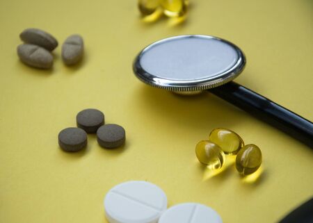 Bunch of pills and capsules and medical stethoscope and blood pressure meter on yellow background, healthcare conceptの写真素材
