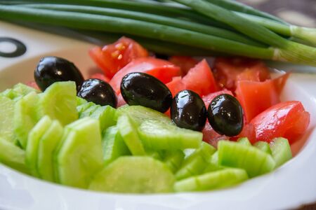 Salad with fresh vegetables, cucumber, tomatoes and black olives in a plate ready for seasoning, ingredients for healthy eatingの写真素材