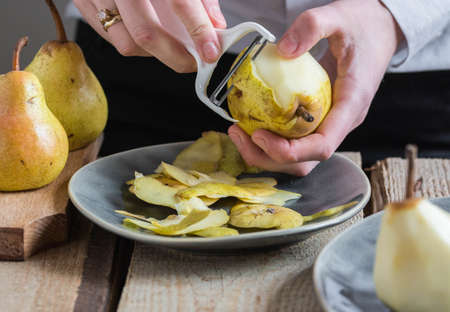 Woman peeling pears with a white vegetable peeler, hands visibleの写真素材