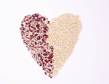 Dry beans of two varieties for vegans in the form of a heart on a white background. Copy space. Flat...