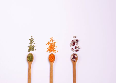 Dry cereals for vegans in wooden spoons: lentils and beans on a white background. Copy space. Flat...