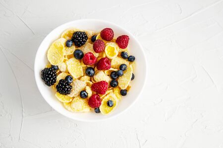 Healthy breakfast with cornflakes in a white plate, berries, milk and coffee on a white background....