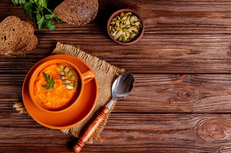 Vegetarian autumn cream soup of pumpkins and carrots with seeds and parsley on a wooden background with copy space, flat lay. Healthy eating concept. Horizontal orientation. View from aboveの写真素材
