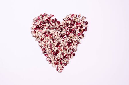 Dry purple beans for vegans in the form of a heart on a white background copy space. Healthy foods high in protein and carbohydrates. View from above.の写真素材