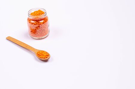 Dry orange lentils for vegans in a wooden spoon and a glass jar on a white background, copy space, place for text. Healthy foods high in protein and carbohydrates. Close-up. Horizontal orientation.の写真素材