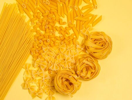 Different types of dry Italian pasta on a yellow background. Spaghetti, farfalle, penne, teatelle, pasta, flat lay, copy space, group. View from aboveの写真素材