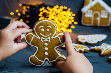 Children's hand holds a Christmas cake in the shape of a man, painted with sugar icing on a dark...